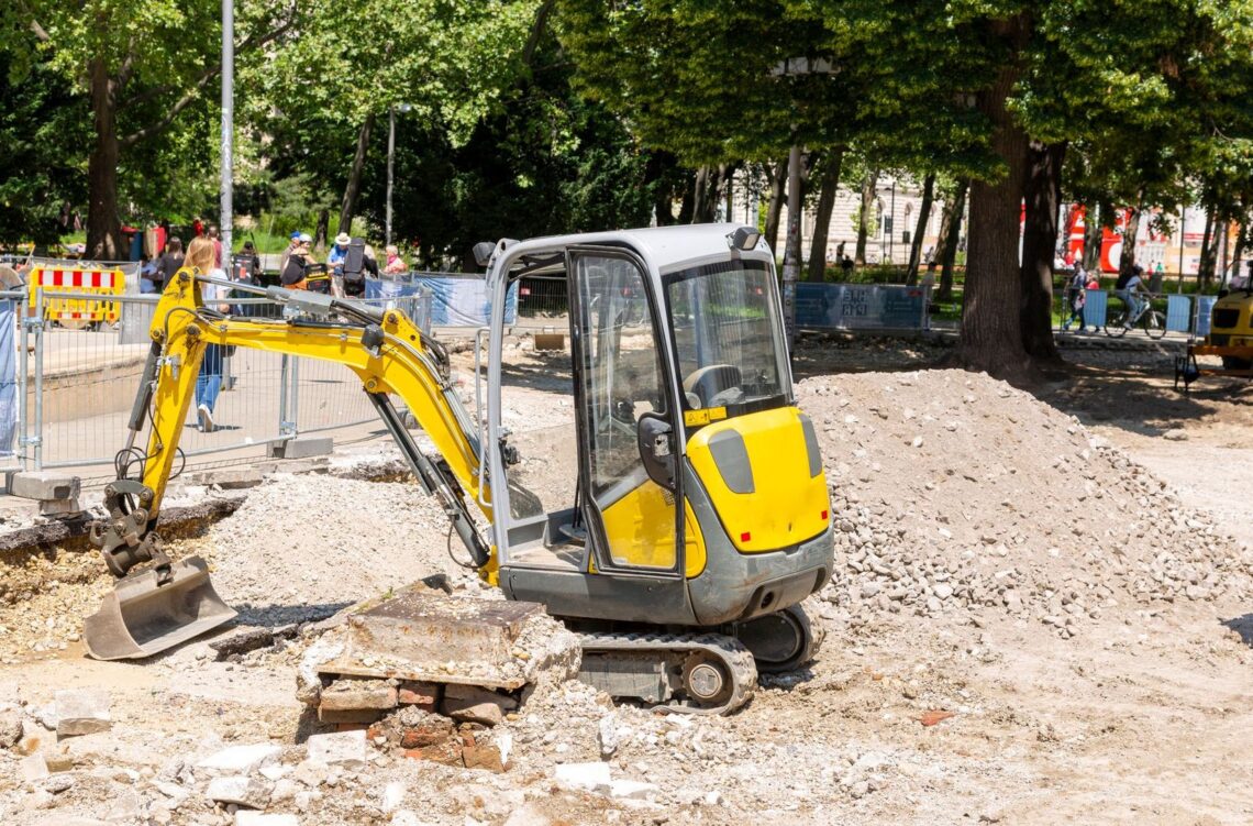 Gul minigrävare på en byggarbetsplats i en parkmiljö